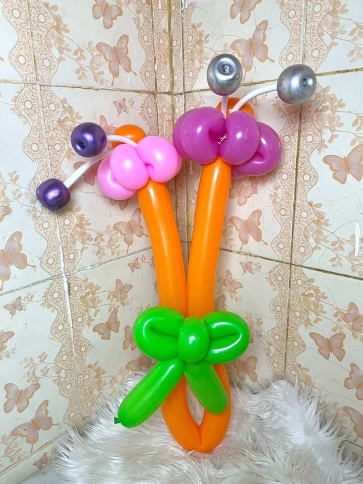 Karakter serangga balon ungu dan oranye dengan pita hijau